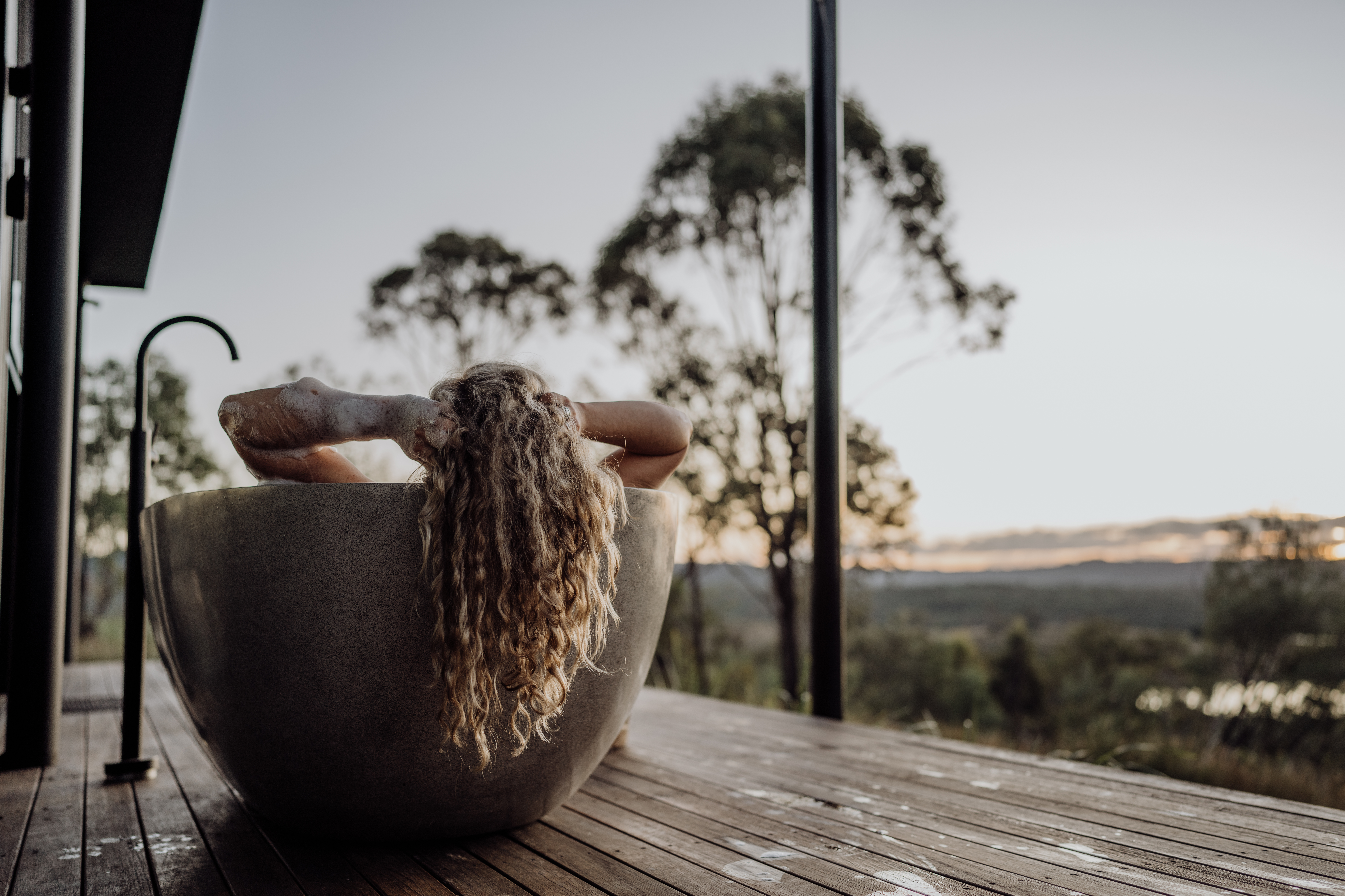 Wander at The Overflow_Lifestyle_112_Credit_Jacqui Faulkner Woman relaxing in the outdoor bath on the Juberra WanderPod deck, Scenic Rim