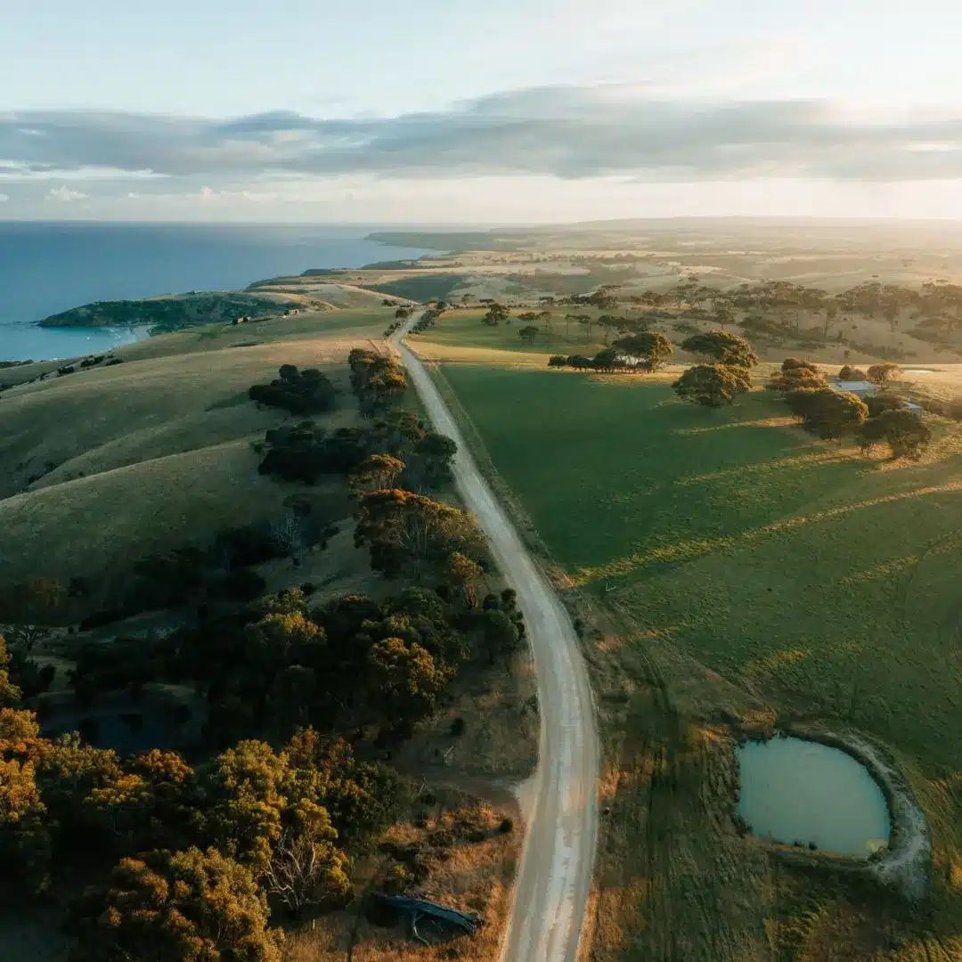 Wander-on-Kangaroo-Island_Location_63_Credit_Remy-Brand-scaled (1) Aerial view of rolling farmland and a gravel road leading to the coast, Kangaroo Island